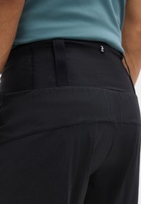 Κοντινό πλάνο ενός ατόμου που φοράει μαύρο αθλητικό παντελόνι με ψηλή μέση και μια μπλε υφασμάτινη μπλούζα μέσα.