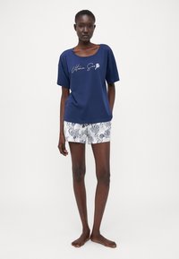 Navyblauwe katoenen t-shirt met een brede halslijn en witte tekstprint, gecombineerd met witte shorts met zwarte zee-thema patronen.