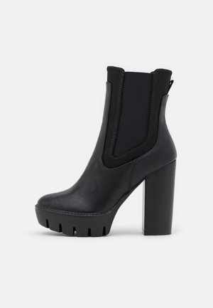 Bottine noire à talon haut épais, avec panneaux latéraux élastiques, finition en cuir lisse et plateforme rainurée pour une meilleure adhérence.