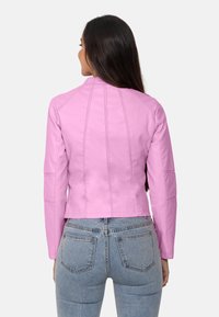 Chaqueta de cuero rosa con un diseño ajustado, detalles en las costuras y mangas largas, combinada con jeans de tiro alto.