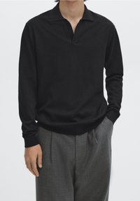 Sort poloshirt med langærmer og v-hals design, lavet af blødt materiale, kombineret med grå skræddersyede bukser med en afslappet pasform.