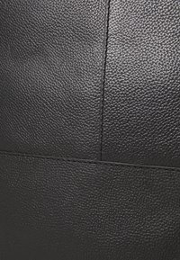 Primo piano di pelle nera testurizzata, con una finitura a ciottoli, cuciture visibili e pannelli rettangolari.