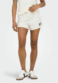 Weiße Handtuch-Shorts aus Frottee mit elastischem Bund und Kordelzug, ausgestattet mit dem schwarzen, gestickten Schriftzug "NYC" an der Seite.