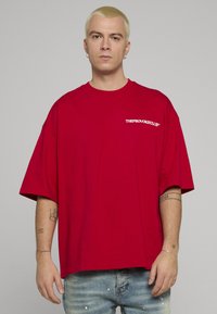 Rød, oversized t-skjorte i bomull med korte ermer og rund hals, med hvit logo på fronten. Brukt sammen med falmede blå jeans.