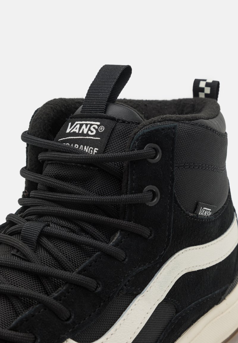 Fekete magas szárú sportcipők, amelyek velúr és hálós anyagok kombinációjából készültek, fekete fűzőkkel, fehér középtalppal és Vans márkajelzéssel a nyelvén.