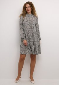 Robe midi florale avec manches longues, col haut et jupe plissée. Le motif présente de petites fleurs bleues et crème sur un fond clair.
