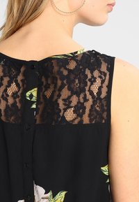 Schwarzes ärmelloses Oberteil mit floralem Druck, Spitze Rückenteil und Knopfverschlüssen entlang des Rückens. Glatte Stofftextur mit floralen Akzenten.