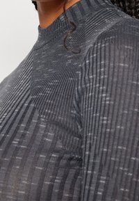 Haut à manches longues côtelé gris foncé avec un col haut. Le tissu texturé présente des motifs de rayures variés pour un intérêt visuel.