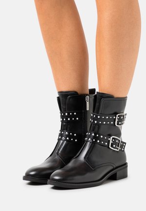 Black leather ankle boots with two studded straps and silver buckles. Features a side zipper and a low block heel for stability.