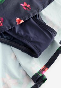 Peldkostīma komplekts ar tumšu ziedu raksta augšdaļu un tumšiem apakšdaļas vienkrāsainā dizainā, izgatavots no elastīga materiāla ar gludu tekstūru un izšūtām detaļām.