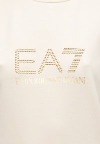 Φούτερ κρεμ χρώματος με χρυσά γράμματα με τρουκς "EA7 EMPORIO ARMANI", με λεία υφή και σχέδιο με στρογγυλή λαιμόκοψη.