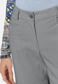 Grijze broek met een gladde textuur, voorzien van een knoop aan de voorkant, riemlussen en zijzakken. Inclusief een patroon op de mouw van het shirt, zichtbaar op de afbeelding.