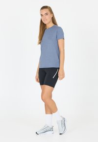 Sininen lyhythihainen t-paita, johon on yhdistetty mustat pyöräilyshortsit, joissa on kyljetasku ja valkoinen reunus. Asua täydentävät vaaleat urheilukengät ja sukat.