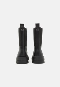 Stivaletti neri alla caviglia con un corpo in pelle lucida, pannelli laterali elastici e una suola in gomma spessa. Presentano un dettaglio del logo impresso sulla suola.