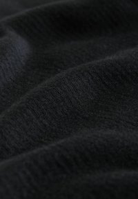 Schwarzer Strickstoff mit weicher Textur und subtiler Rippstruktur, der sichtbare Falten und unterschiedliche Lichtreflexion aufweist.