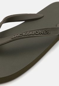 Mørkegrøn flip-flop med en tekstureret fodseng, kontrastfarvede glatte stropper og præget logo-detalje på stroppen.