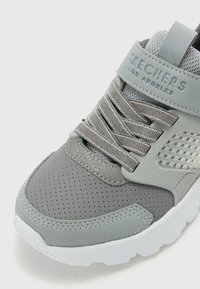 Grå Skechers sneakers med mesh-paneler, teksturerte aksenter, polstret krage og gummisåle. Har en logo og kontrasterende snøring.