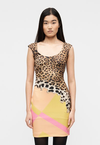 Femme portant une robe sans manches avec un haut à imprimé léopard et une jupe à blocs de couleurs en beige, jaune et rose, se tenant devant un fond uni.
