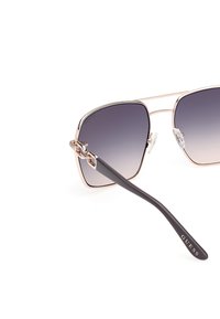 Neliömäiset aurinkolasit, joissa on gradienttiset linssit, ruusukultainen metallirunko ja tummanruskeat asetaattitele. Erottuva logo varressa.