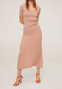 Prachově růžový žebrovaný dvoudílný set se přiléhavým tričkem s krátkým rukávem a volnou midi sukňou. Doplněno oranžovými sandály na řemínky.