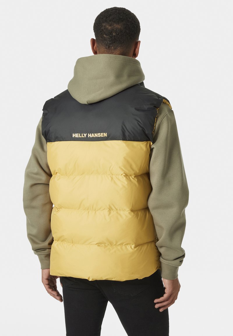Steppweste mit schwarzem Oberteil und gelbem unteren Abschnitt, mit einem Reißverschluss und dem "Helly Hansen"-Logo, getragen über einem grünen Hoodie.