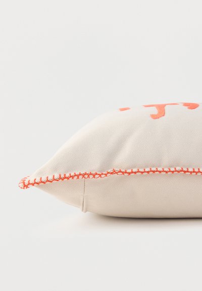 Coussin beige avec broderie orange et couture orange assortie sur fond clair, vu de côté.