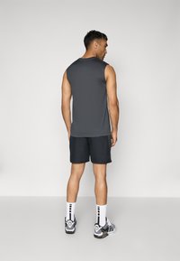 Camisa atlética sem mangas em cinza escuro, combinada com calções pretos. Apresenta um tecido macio, um corte descontraído e um design leve.