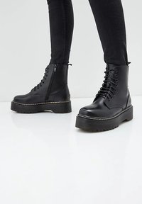 Bottines noires avec une semelle plateforme épaisse, tige en cuir lisse, lacets à l'avant, fermeture éclair sur le côté et semelle en caoutchouc texturée pour une meilleure adhérence.