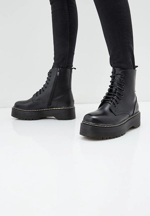 Bottines noires avec une semelle plateforme épaisse, tige en cuir lisse, lacets à l'avant, fermeture éclair sur le côté et semelle en caoutchouc texturée pour une meilleure adhérence.