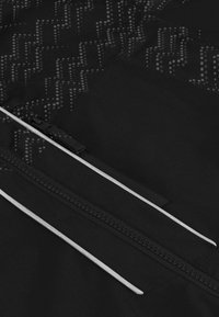 Schwarzer Stoff mit einem subtilen geometrischen Muster. Enthält kontrastierende weiße Reißverschlüsse und eine Reißverschlusstasche. Glatte Textur, leichtes Design.