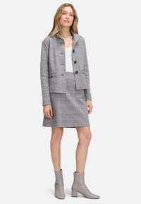 Grijze geruite blazer met vier knopen, twee voorkruipockets en een cropped fit, gecombineerd met een bijpassende geruite rok tot de knie en grijze enkellaarzen.