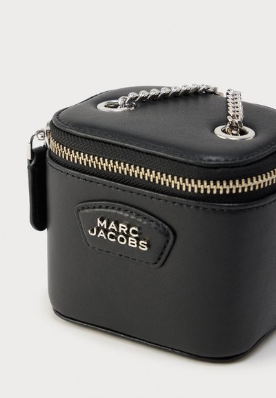 Μαύρη δερμάτινη τετράγωνη τσάντα με φερμουάρ, αλυσίδα λαβής και χρυσά μεταλλικά στοιχεία· διαθέτει ανάγλυφο λογότυπο της μάρκας σε δερμάτινο πάτς.