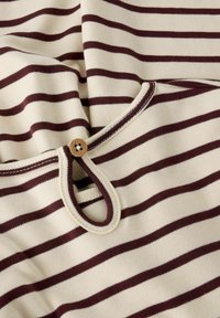 Kokvilnas tops ar krēmkrāsas un bordo horizontālām svītrām, ar noapaļotu kakla izgriezumu un koka pogu detalizāciju pie apkakles.