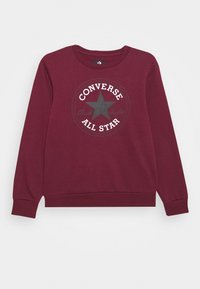 Felpa bordeaux con un logo rotondo che presenta una stella nera centrale e testo bianco che riporta "CONVERSE ALL STAR" e "Chuck Taylor". Texture morbida.