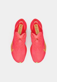 Chaussures de sport rose vif avec une tige texturée, une silhouette structurée et une semelle verte. Présente des accents orange et un système de laçage traditionnel.