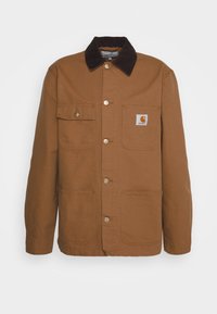 Giacca da lavoro marrone con colletto in velluto a coste, quattro tasche frontali e bottoni metallici. Logo di marca distintivo sulla tasca del petto.