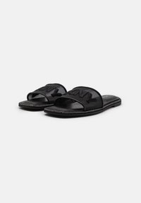 Black slip-on sandals feature a textured upper with cut-out detailing and a smooth leather footbed. The sole has minimal edging.
