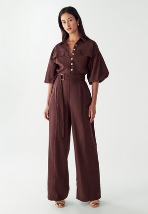Brauner, knöpfbarer Overall mit kurzen Puffärmeln, tailliertem Bund, weitem Bein und zwei Brusttaschen. Glattes Material mit mattem Finish.
