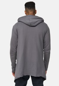 Sudadera con capucha gris y un dobladillo largo y asimétrico. Hecha de una tela suave, presenta un corte relajado y un diseño simple y minimalista.