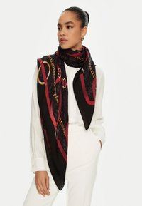 Foulard en soie avec un fond noir et des motifs de chaînes rouges et dorées, drapé élégamment autour du cou, avec une texture lisse et brillante.
