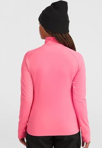 Chaqueta de manga larga rosa hecha de material suave y elástico, con un cuello alto y mangas raglán; combinada con un gorro de punto negro.