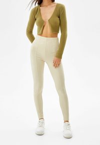 Cárdigan cropped de punto acanalado en verde oliva combinado con leggings acanalados de talle alto en beige, completado con zapatillas blancas.