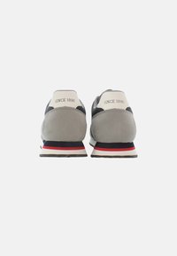 Sneaker in suede grigio e mesh con un accento bianco sul tallone, caratterizzati dal testo "SINCE 1890" e una suola a righe rosse, bianche e blu navy.