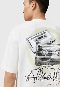 Tricou alb din bumbac cu un design grafic reprezentând casete audio, cu textul "MESAJ PENTRU UN VIITOR" și un accent cursiv negru "Allsaints".