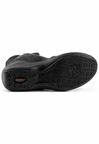 Zapato de cuero negro con una textura suave y una suela de goma que presenta un logotipo impreso y una ligera curvatura en el área del talón.