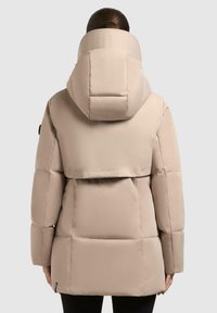Giacca puffer beige con colletto alto, caratterizzata da un motivo a cuciture orizzontali e una texture liscia, progettata per il calore e l'isolamento.