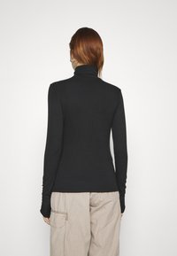 Schwarzer, gerippter Rollkragenpullover mit langen Ärmeln, figurbetontem Design und glatter Textur, kombiniert mit hellbeigen Cargo-Hosen.