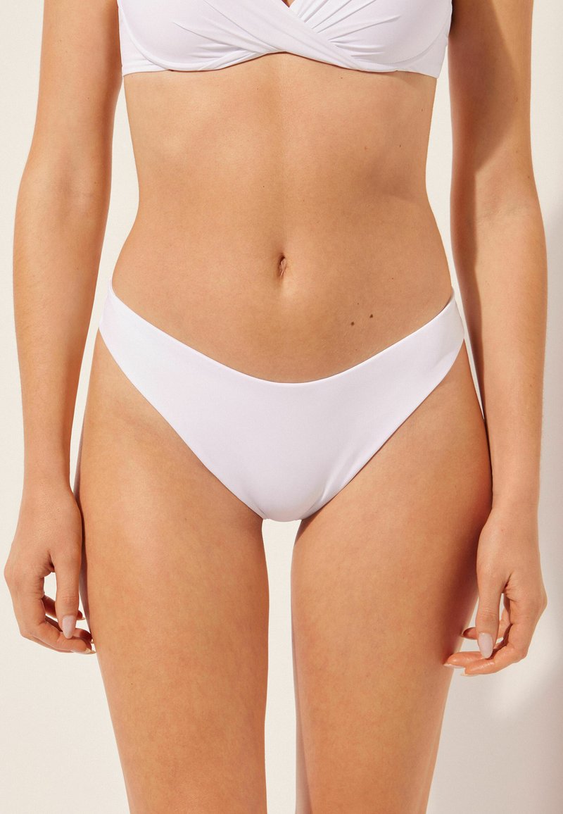 Vita bikiniunderdel med en slät, elastisk textur. Den har en lågt skuren design och minimalistisk täckning. Ingen synlig hårdvara eller mönster.