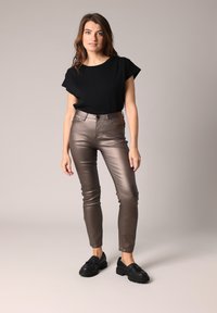 Zwarte top met korte mouwen, glanzende bronzen strakke broek en zwarte schoenen. Gladde textuur met subtiele glans, op maat gemaakt pasvorm die de silhouet accentueert.