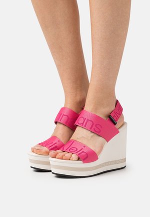 Růžové wedges sandály se širokými textilními popruhy s logem "Calvin Klein Jeans", bílou platformou a texturovanou gumovou podrážkou.